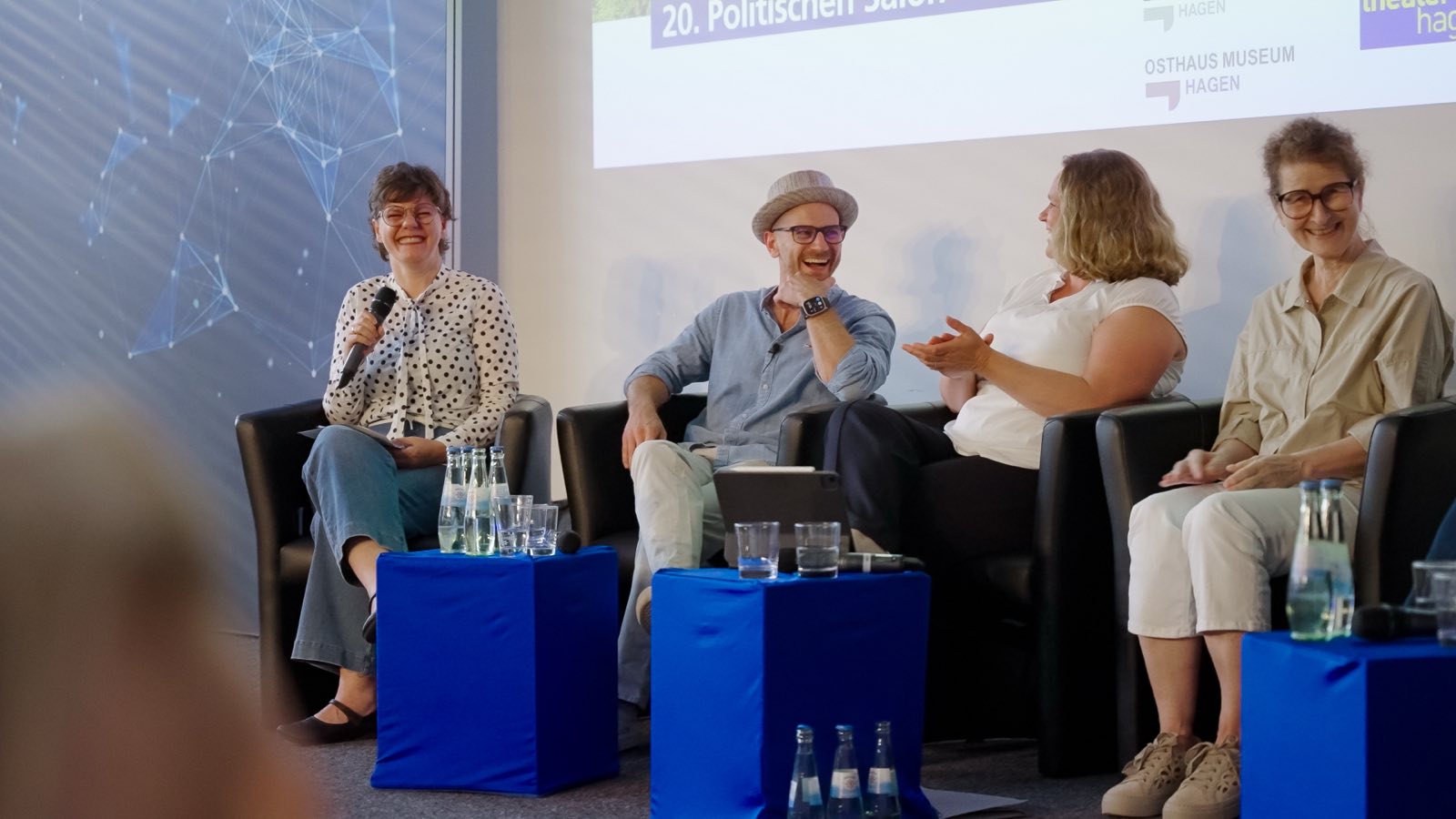 Marcel Colley lacht während einer Podiumsdiskussion, neben ihm drei weitere Panelistinnen